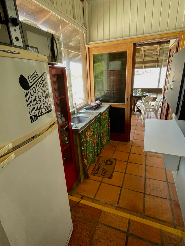 Cozinha com geladeira, micro-ondas e pia, com porta para a varanda